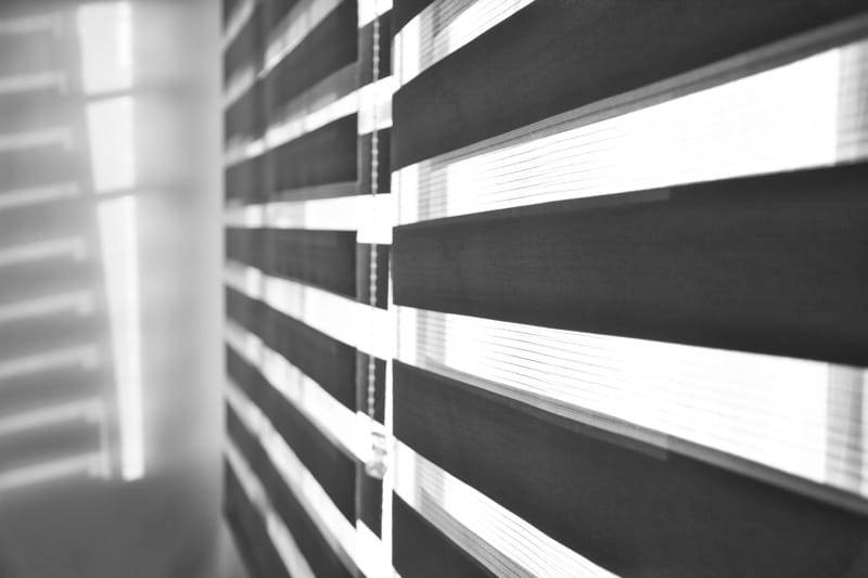 sun shining through window blinds throwing shadows wall black white